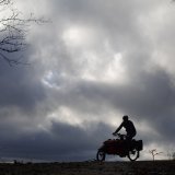 Die Silhouette einer Person auf einem Lastenrad auf dem Horizont vor dunklen Wolken.