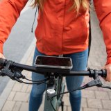 Ein Smartphone ist mittig auf dem Lenker eines Fahrrades montiert. Eine Person mit roter Jacke greift den Lenker.