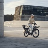 Eine Person auf einem E-Bike mit längerem Gepäckträger vor moderner Architektur.