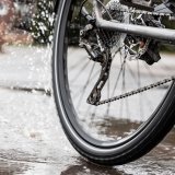 Bild des Hinterrades eines Fahrrades, dass durch eine Pfütze fährt. Vom Reifen spritzt Wasser.