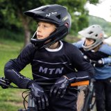 Ein Junge mit Fullface-Helm lehnt auf dem Lenker eines Mountainbikes und schaut sich um.