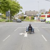 Eine Person auf einem Liegedreirad fährt auf einer Abbiegespur auf eine Straßenkreuzung.