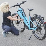 Eine Frau kniet neben einem E-Bike und setzt den Akku in den Rahmen ein.
