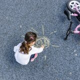 Ein Kind hockt neben einem Laufrad und malt mit Kreide auf dem Boden.
