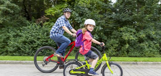 Ein Mann und ein Kind fahren auf Fahrrädern einen gepflasterten Weg entlang.