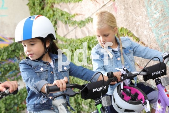 Zwei Mädchen stehen mit Fahrrädern herum, eine mit Helm auf den Kopf und eine mit dem Helm am Lenker hängend.