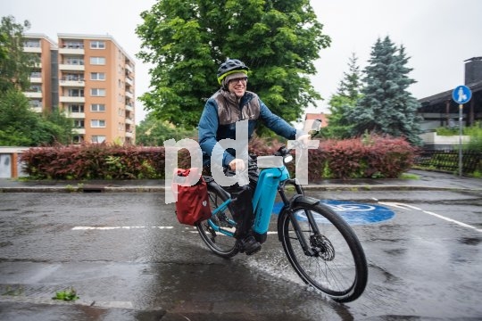 Ein Mann fährt bei Regen auf einem E-Bike durch ein Wohngebiet.