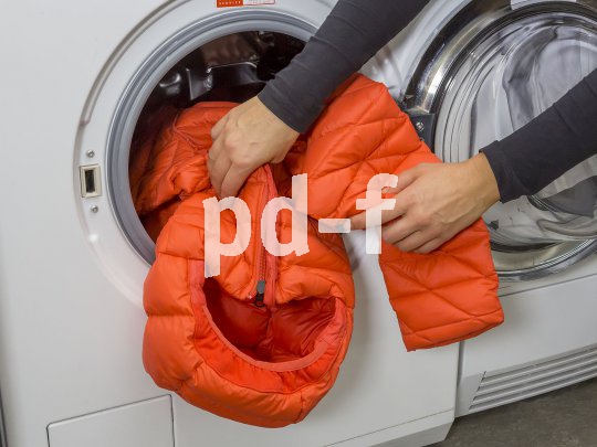 Eine Person steckt eine wattierte Jacke in eine Waschmaschine.
