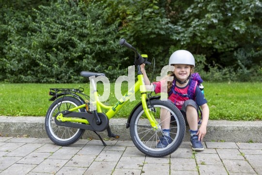Ein Kind sitzt neben einem grünen Kinderrad auf einer Bordsteinkante.