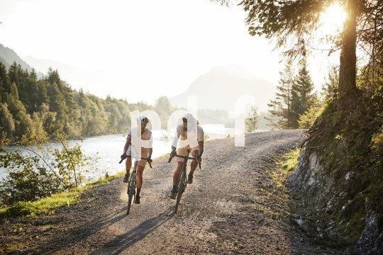 Zwei Personen fahren mit Fahrrädern eine Schotterstraße am Rande eines Flusses.