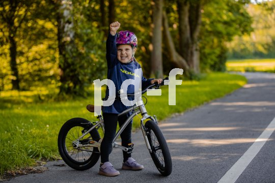 Ein Kind steht mit einem Fahrrad am Straßenrand und streckt jubelnd eine Faust in die Höhe.