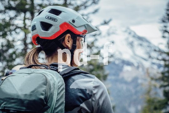 Frau mit Mountainbike-Helm und Rucksack blickt auf Berg.