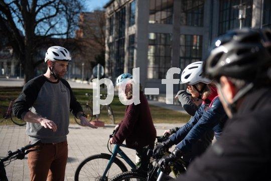 Ein Mann steht vor einer Gruppe Radfahrer:innen und erklärt etwas mit den Händen.