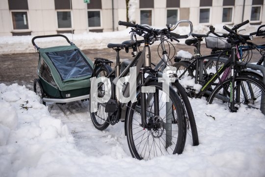 Ein Fahrrad mit Anhänger an einem Abstellbügel. Im Bereich der Stellfläche liegt weniger Schnee als daneben.