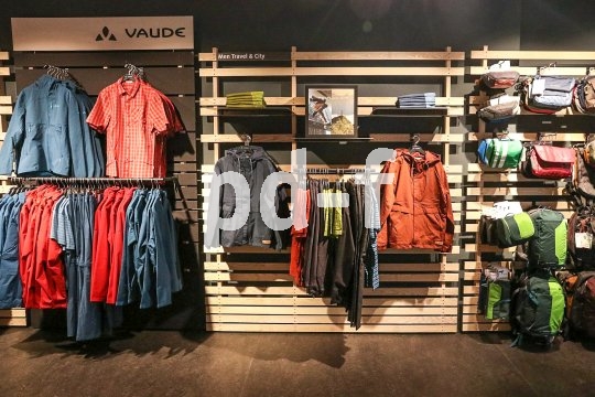 Eine Produktpräsentationswand mit Jacken, Oberteilen und Taschen der Firma Vaude.