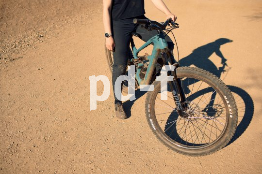 Eine Person steht mit einem Mountainbike auf einer sandigen Fläche.