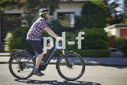 Ein lächelnder Mann fährt auf einem E-Bike durch ein Wohngebiet.