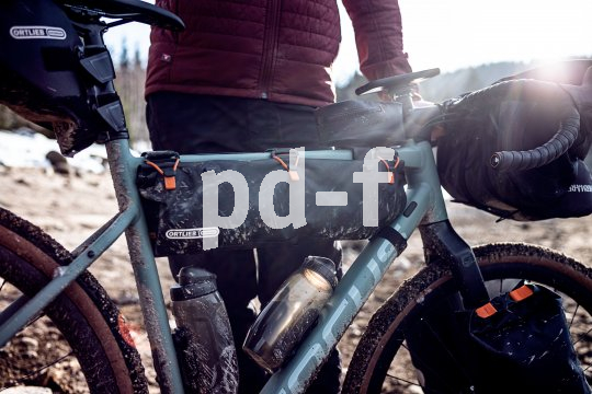 Eine Person hält ein schmutziges Fahrrad mit wasserdichten Taschen der Firma Ortlieb vor sich.