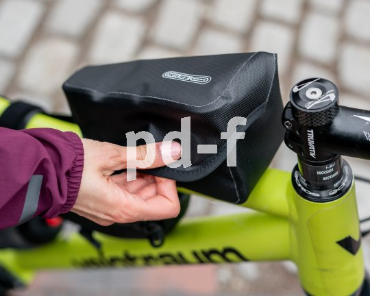 Eine Person öffnet oder schließt eine kleine Fahrradtasche auf dem Oberrohr eines Fahrrades.