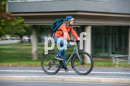 Eine Frau mit einem Rucksack fährt auf einem Fahrrad auf einem Radweg in der Stadt.