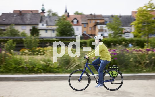 Mann fährt mit Fahrrad vor Blumen.