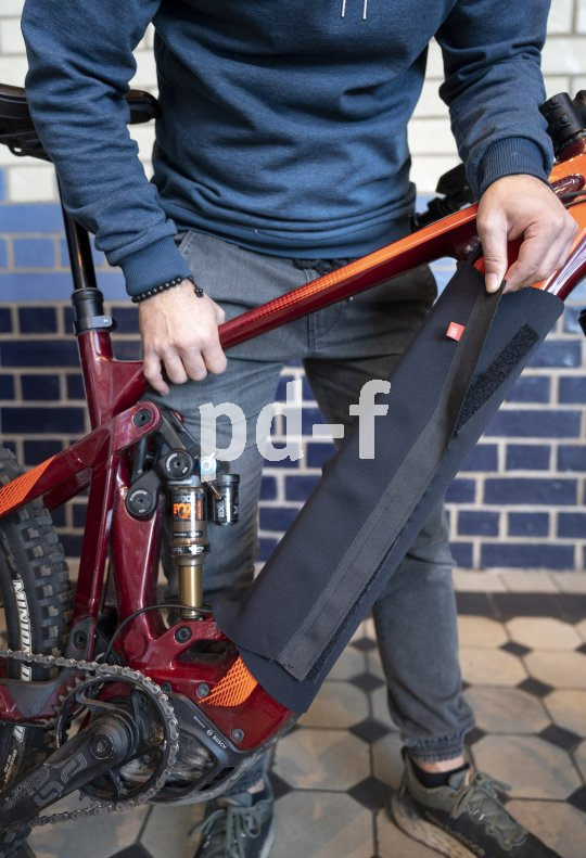 Eine Person wickelt eine Schutzhülle mit Klettverschluss um das Unterrohr und damit den Akku eines E-Bikes.