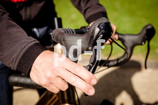 Die rechte Hand einer Person an einem Rennradlenker mit zwei Fingern am Bremshebel.