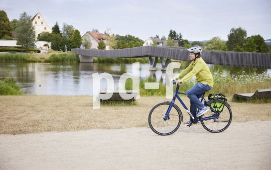 Mann fährt mit Fahrrad vor See und Brücke