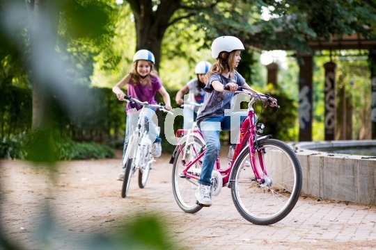 Drei Kinder fahren in einem Park Fahrrad.
