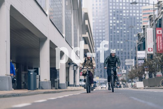 Zwei Personen fahren auf Fahrrädern in einer Großstadt auf die Kamera zu.