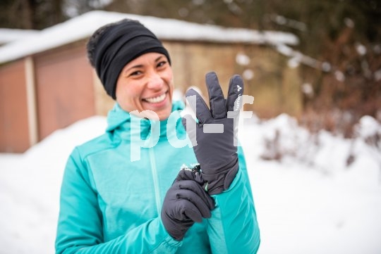 Eine lachende Frau zieht sich in verschneiter Umgebung Handschuhe an.