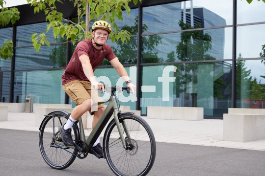 Ein Mann fährt auf einem E-Bike vor einem Gebäude mit Glasfassade entlang.