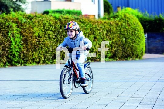 Ein Kind mit buntem Helm fährt mit einem Fahrrad über einen Platz.