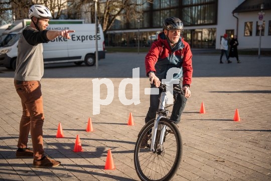 Ein Mann fährt mit einem E-Bike zwischen orangefarbenen Hütchen während ein zweiter Mann daneben steht und ihm die Richtung weist.
