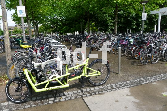 Ein Lastenrad mit einem Faltrad auf der Ladefläche, abgestellt am Rande einer großen Stellfläche für Fahrräder.