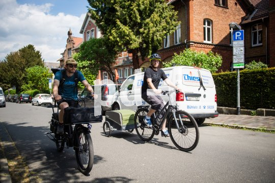Ein Radfahrer auf einem Lastenrad und einer mit Anhänger fahren nebeneinander eine innerstädtische Straße entlang.