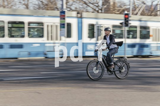 Ein Mann fährt auf einem E-Bike durch die Stadt. Im Hintergrund: eine weiß-blaue Straßenbahn.