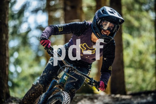 Frau mit Helm und Brille fährt mit Mountainbike durch Wald 