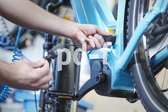 Die Hände einer Person, die ein Ladekabel am Rahmen eines E-Bikes anschließt oder abzieht.