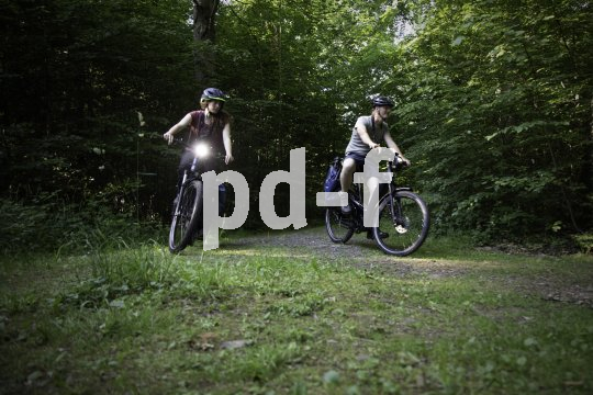Zwei Personen fahren auf E-Bikes durch einen Wald.