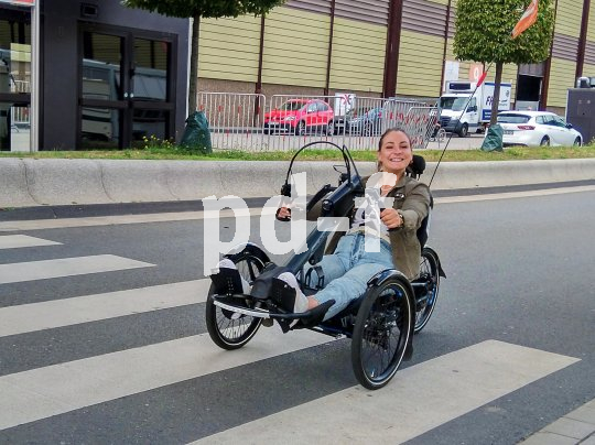 Die ehemalige Profifahrerin Kristina Vogel fährt mit einem Handbike auf einer Straße. Das Handbike hat vorne zwei Räder, hinten eins und wird mit Handkurbeln angetrieben.
