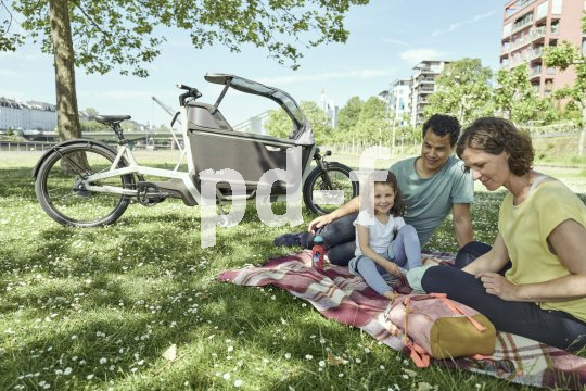 Eine Familie beim Picknick; im Hintergrund steht ein Lastenrad.