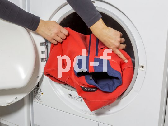 Eine Person steckt eine Jacke in eine Waschmaschine.