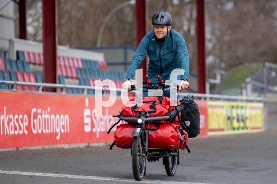 Ein Mann fährt mit einem Lastenrad vor den Zuschauerrängen einer Radrennbahn entlang.