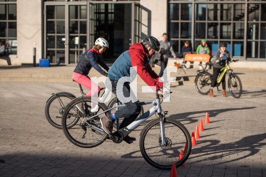 Ein Mann bremst sein E-Bike zwischen orangefarbenen Hütchen. Das Hinterrad hebt dabei vom Boden ab. Im Hintergrund schauen mehrere Personen zu.