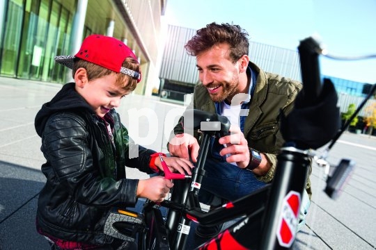 Ein Mann und ein Junge hocken neben einem Kinderrad. Der Junge hat ein Werkzeug in der Hand.