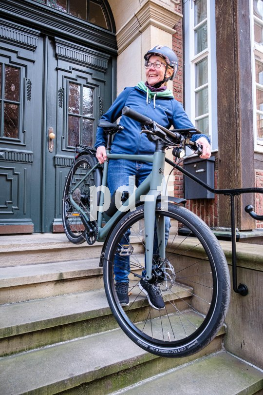 Eine Frau trägt ein Fahrrad die Treppe vor einer Haustür hinab.