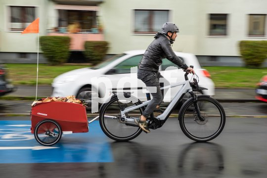Ein Mann fährt auf einer Fahrradstraße mit einem E-Bike durch ein Wohngebiet. Am Rad hängt ein roter Anhänger.