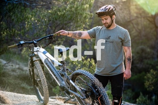 Ein Mann steht in der Natur neben einem E-Bike und betrachtet es.