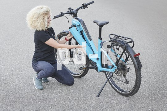 Eine Frau kniet neben einem E-Bike und setzt den Akku in den Rahmen ein.